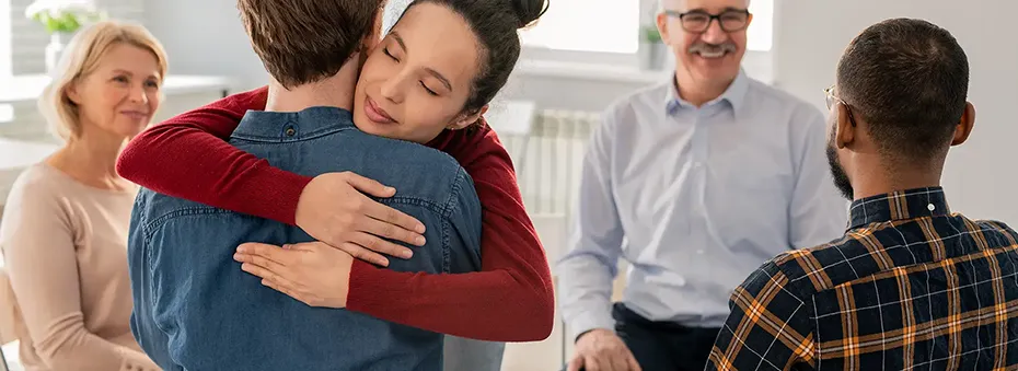 Young supportive woman embracing one psychological session groupmates.